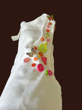 Load image into Gallery viewer, A close-up of a white ribbed ladies decorated with colorful buttons and butterfly embellishments against a dark blue background.
